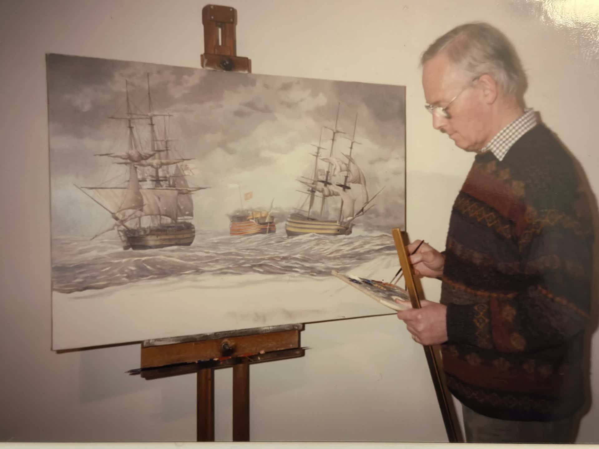 El pintor, paleta en mano, ante el lienzo de tres navíos aún en curso.