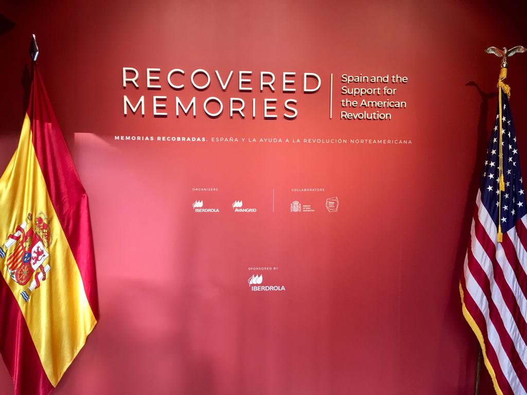 Muro rojo con el título «Recovered Memories» en letras metálicas, flanqueado por la bandera de España y la de los Estados Unidos