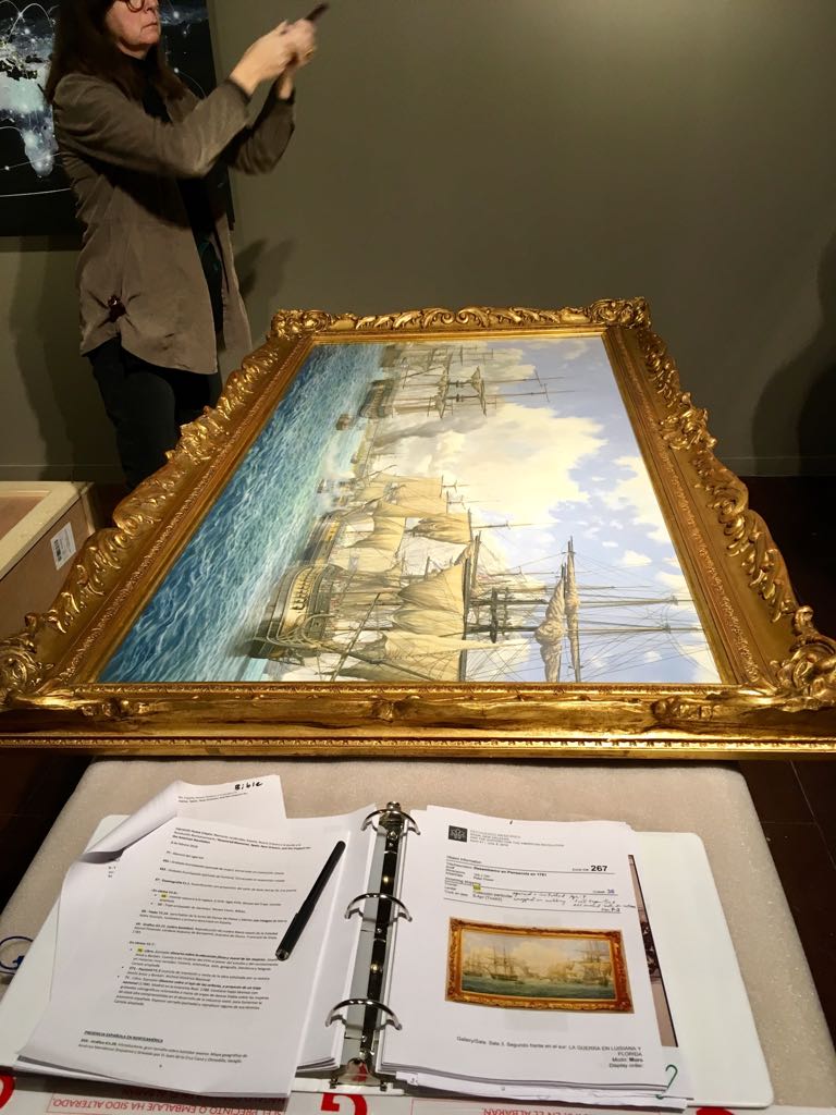 Una conservadora fotografía el óleo de Pensacola apoyado durante el montaje; en primer plano, la carpeta abierta con la ficha de obra número 267
