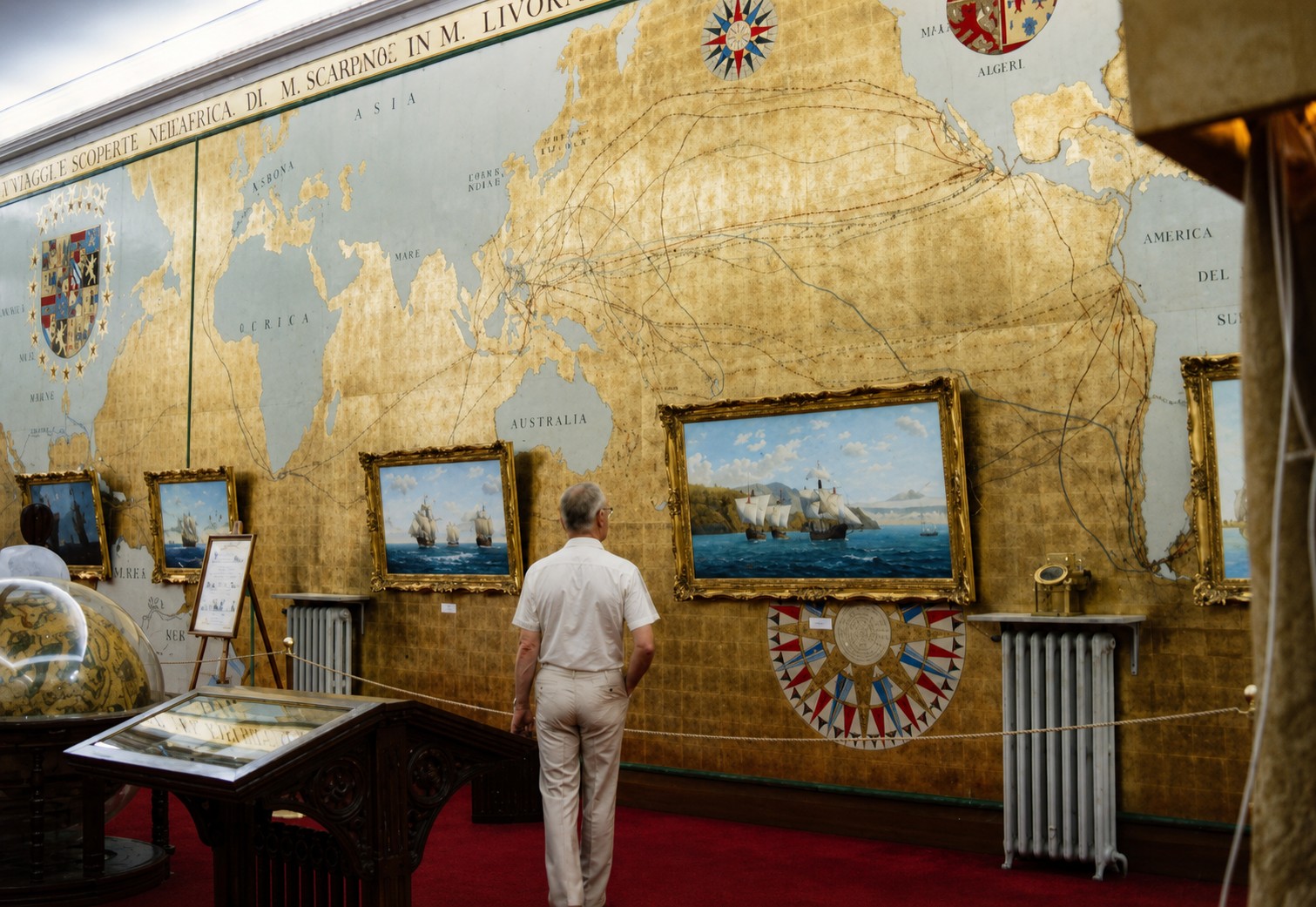 Vista de la sala con los lienzos en sus marcos dorados junto a la esfera y la vitrina de cartografía histórica.