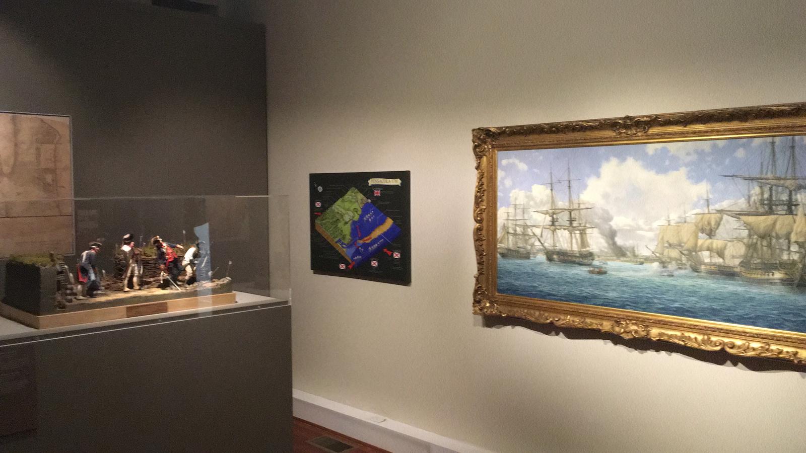 Sala de museo con el óleo de Pensacola en su marco dorado a la derecha, un plano del sitio en el centro y un diorama de soldados en vitrina a la izquierda